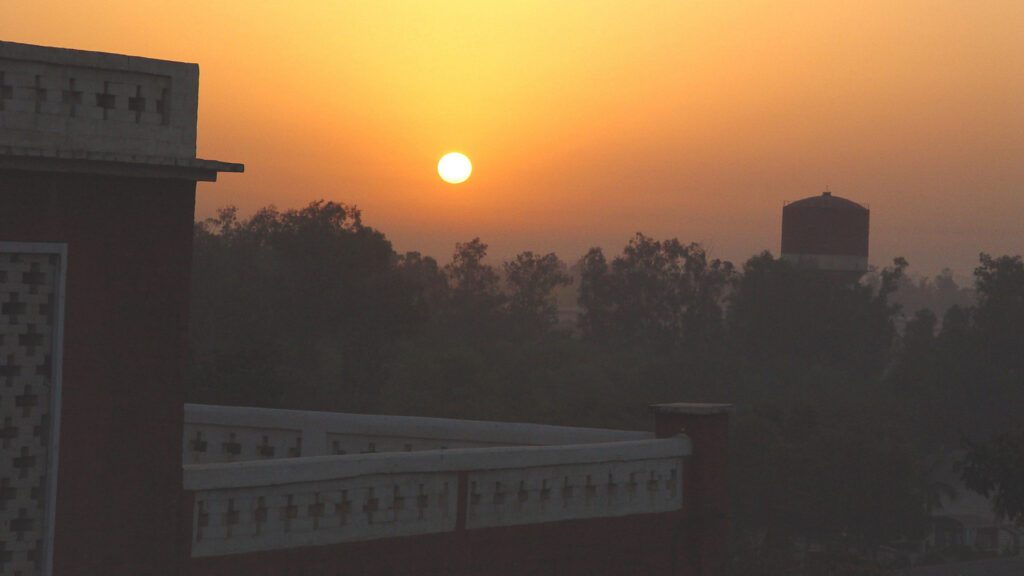 Sun rising over a city skyline with silhouetted buildings and trees