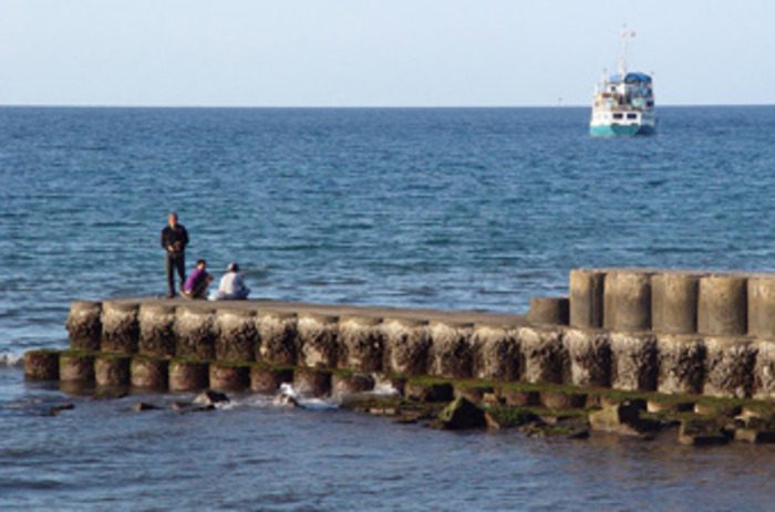 People standing on the Singaraja wharf with fishing boat offshore in Bali