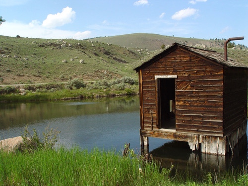 Weathered wooden cabin standing over a pond in the Yellowstone backcountry.