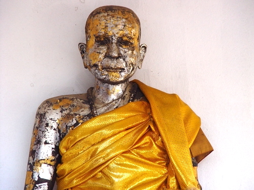 Buddhist monk statue covered with gold leaf and draped in saffron robes.