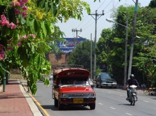Traditional red songthaew taxi driving along a street in Chiang Mai, Thailand.
