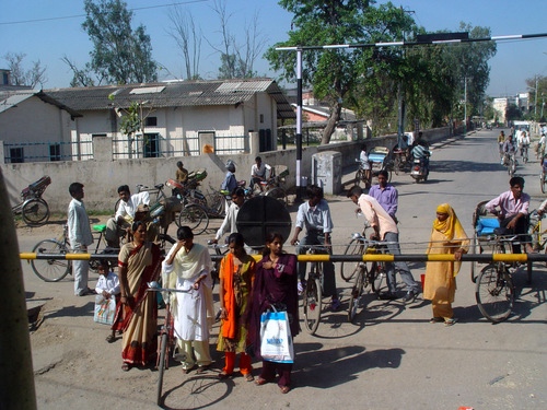 People waiting with bicycles and rickshaws at a railway crossing in northern India.