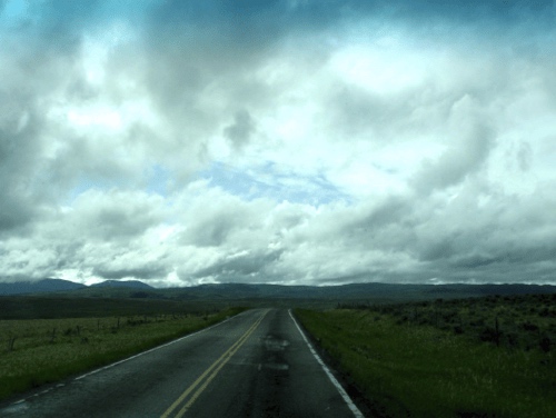 A lonely highway stretching across the open plains of Montana beneath dramatic storm clouds.