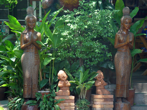 Traditional Thai statues displayed among tropical plants and garden landscaping.