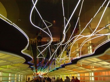 Travelers walking beneath the illuminated Sky's the Limit sculpture at O'Hare Airport.