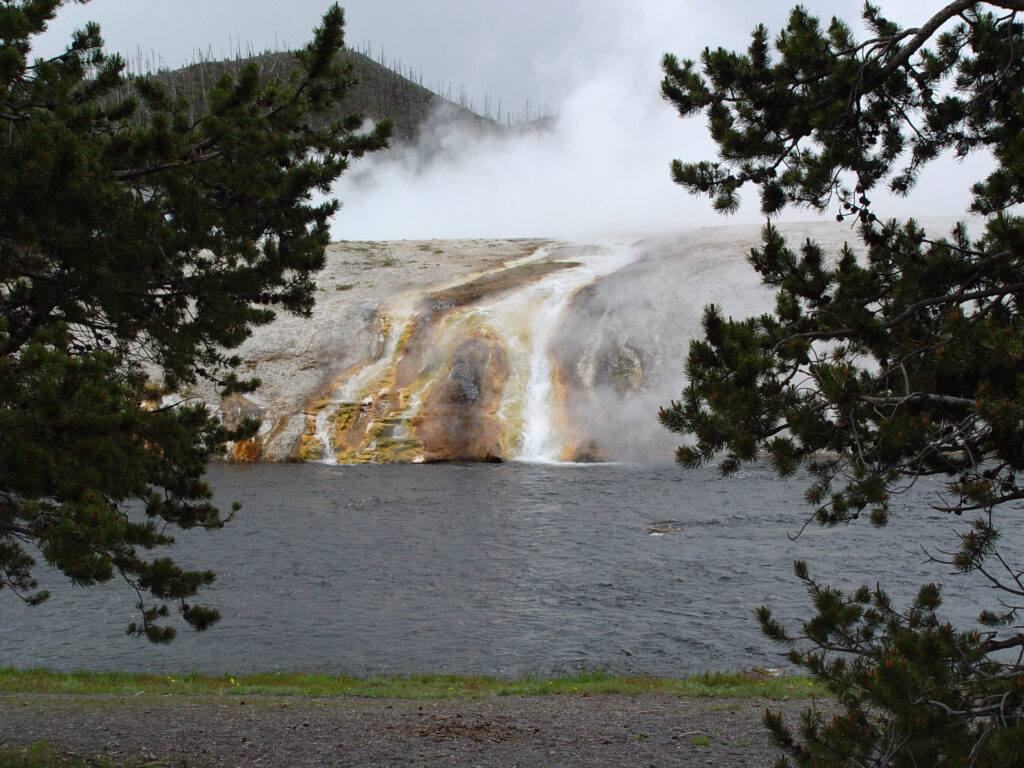 Steam rising from a colorful thermal spring beside a Yellowstone river.